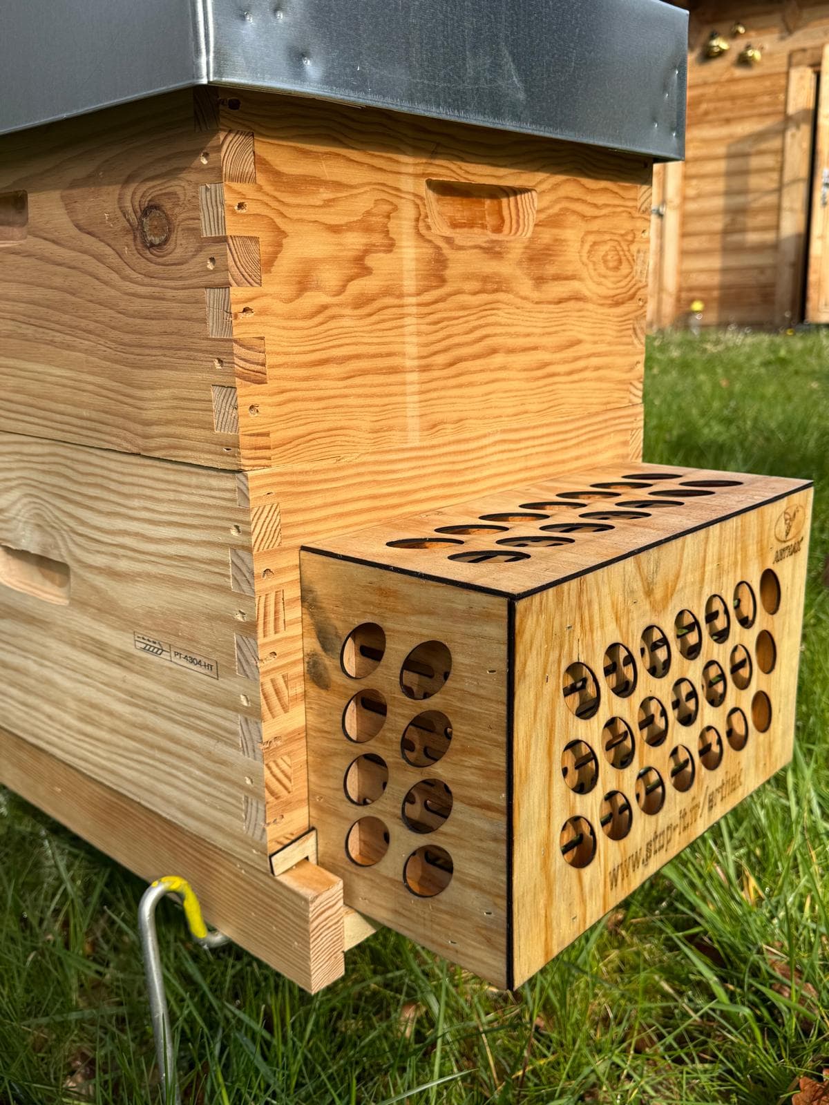 Wooden beehive with a metal lid and a wooden box attachment featuring circular holes.