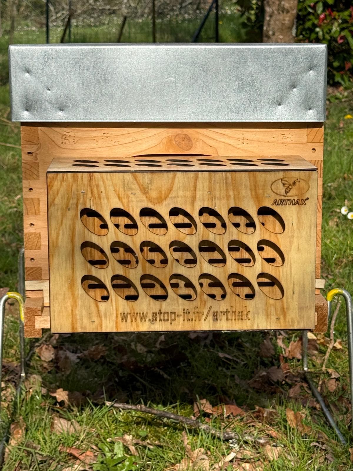 Wooden beehive with a metal roof and a wooden hornet trap attached to the entrance.