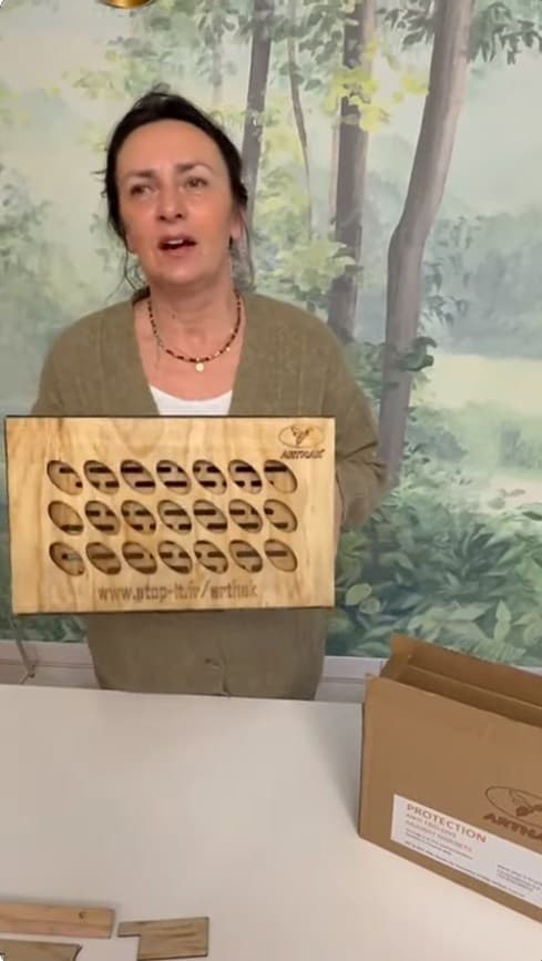 Woman holding a wooden Arthak board with oval cutouts against a forest-themed wall mural.